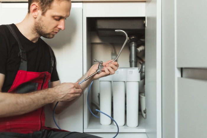 technician working on a water filtration system installation under a kitchen cabinet