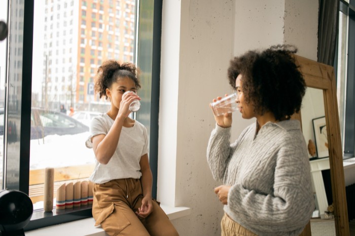 A mother and daughter enjoying clean filtered water indoors, showcasing the health benefits of water purification
