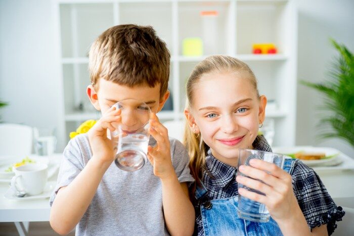 Kids drinking purified water from a reverse osmosis system at home
